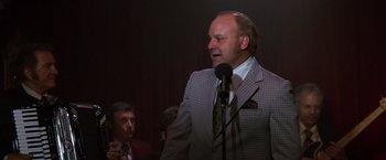 Movie still from “Man on the Moon” (1999), directed by Milos Forman – A man standing in front of a microphone in front of another man; Medium shot, Over the shoulder angle