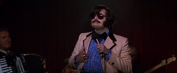 Movie still from “Man on the Moon” (1999), directed by Milos Forman – A man in a suit and bow tie holding a microphone; Medium shot, Low angle