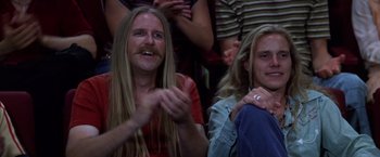 Movie still from “Man on the Moon” (1999), directed by Milos Forman – Two people with long hair and a beard are sitting in a crowd; Medium shot, High angle