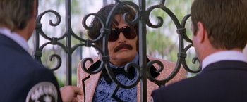 Movie still from “Man on the Moon” (1999), directed by Milos Forman – A man with a mustache wearing a suit and sunglasses; Medium shot, Over the shoulder angle