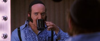 Movie still from “Man on the Moon” (1999), directed by Milos Forman – A man with a beard drinking from a black mug; Close Up shot, Over the shoulder angle