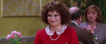 Movie still from “Man on the Moon” (1999), directed by Milos Forman – A woman with curly hair wearing a red dress and pearl necklace; Close Up shot, Over the shoulder angle