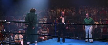 Movie still from “Man on the Moon” (1999), directed by Milos Forman – A man in a boxing ring holding a microphone; Wide shot, Low angle
