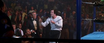 Movie still from “Man on the Moon” (1999), directed by Milos Forman – A man in white shirt holding a microphone in front of a crowd of onlookers; Medium shot, Low angle