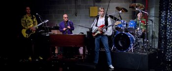 Movie still from “Man on the Moon” (1999), directed by Milos Forman – A man playing a guitar while another man plays a piano; Wide shot, Low angle