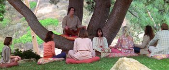 Movie still from “Man on the Moon” (1999), directed by Milos Forman – A group of people sitting on the ground under a tree; Wide shot, High angle