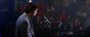 Movie still from “Man on the Moon” (1999), directed by Milos Forman – A man standing at a microphone in front of a crowd; Medium shot, Over the shoulder angle
