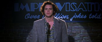 Movie still from “Man on the Moon” (1999), directed by Milos Forman – A man standing in front of a microphone on a stage; Close Up shot, Over the shoulder angle
