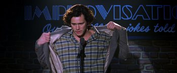 Movie still from “Man on the Moon” (1999), directed by Milos Forman – A man standing up with a microphone in front of a microphone stand; Medium shot, Low angle