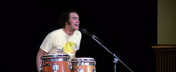 Movie still from “Man on the Moon” (1999), directed by Milos Forman – A man standing at a microphone with two drums; Medium shot, Low angle