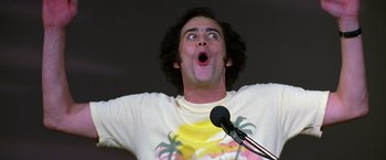 Movie still from “Man on the Moon” (1999), directed by Milos Forman – A man with curly brown hair is standing at a microphone; Close Up shot, Low angle