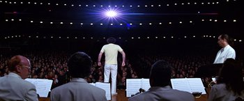 Movie still from “Man on the Moon” (1999), directed by Milos Forman – A man standing in front of an audience with musical instruments; Extreme Wide shot, Low angle