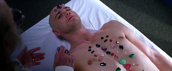 Movie still from “Man on the Moon” (1999), directed by Milos Forman – A man is laying on a bed with many stones on his chest; Close Up shot, Overhead angle