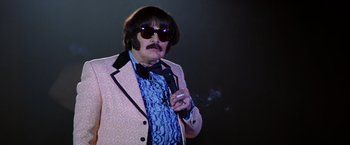 Movie still from “Man on the Moon” (1999), directed by Milos Forman – A man in a suit and sunglasses smoking a cigarette; Medium shot, Low angle