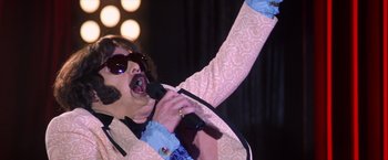 Movie still from “Man on the Moon” (1999), directed by Milos Forman – A man in a pink jacket is singing into a microphone; Close Up shot, Low angle