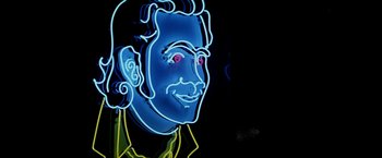 Movie still from “Man on the Moon” (1999), directed by Milos Forman – A neon sign of a man's face with red eyes; Extreme Close Up shot, Overhead angle