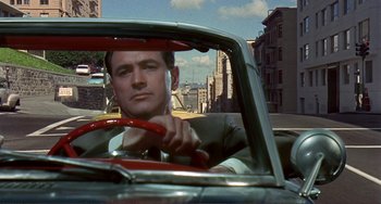 Movie still from “Man's Favorite Sport?” (1964), directed by Howard Hawks – A man in a suit driving a car on the street; Medium shot, Low angle