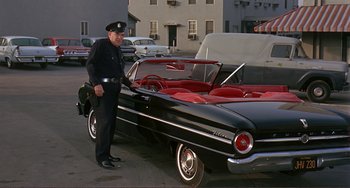 Movie still from “Man's Favorite Sport?” (1964), directed by Howard Hawks – A man standing next to an antique car; Wide shot, Low angle