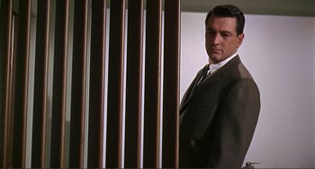 Movie still from “Man's Favorite Sport?” (1964), directed by Howard Hawks – A man in a suit standing next to a wooden fence; Medium shot, Low angle