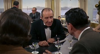 Movie still from “Man's Favorite Sport?” (1964), directed by Howard Hawks – An older man sitting at a table in front of two other people; Medium shot, Over the shoulder angle