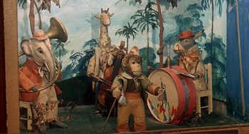Movie still from “Man's Favorite Sport?” (1964), directed by Howard Hawks – A stuffed monkey is holding a violin in front of a mural of giraffes; Wide shot, High angle