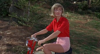 Movie still from “Man's Favorite Sport?” (1964), directed by Howard Hawks – A woman sitting on a red bike in the woods; Medium shot, Low angle