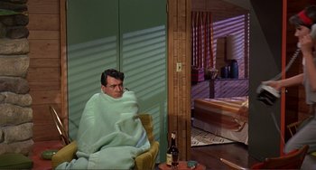 Movie still from “Man's Favorite Sport?” (1964), directed by Howard Hawks – A man wrapped in a blanket sitting in a chair in front of a tub; Wide shot, High angle