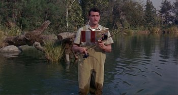 Movie still from “Man's Favorite Sport?” (1964), directed by Howard Hawks – A man standing in the water holding two fishing rods; Medium shot, High angle