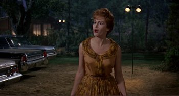 Movie still from “Man's Favorite Sport?” (1964), directed by Howard Hawks – A woman in a brown dress standing next to a car; Medium shot, Low angle