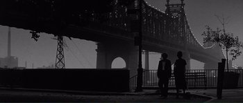 Movie still from “Manhattan” (1979), directed by Woody Allen – A man standing on a sidewalk next to a railing; Wide shot, Low angle