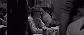 Movie still from “Manhattan” (1979), directed by Woody Allen – A man sitting at a table in front of other people; Close Up shot, Over the shoulder angle