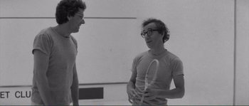 Movie still from “Manhattan” (1979), directed by Woody Allen – Two men talking to each other while holding a tennis racquet; Medium shot, Over the shoulder angle