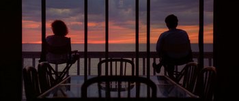 Movie still from “Manhunter” (1986), directed by Michael Mann – Two people sitting at a table near the ocean at sunset; Extreme Wide shot, Over the shoulder angle