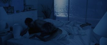 Movie still from “Manhunter” (1986), directed by Michael Mann – A man and a woman laying in a bed in front of a window at night; Wide shot, High angle
