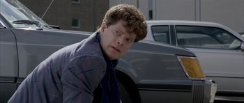 Movie still from “Manhunter” (1986), directed by Michael Mann – A man in a jacket and tie leaning against a car; Close Up shot, Over the shoulder angle