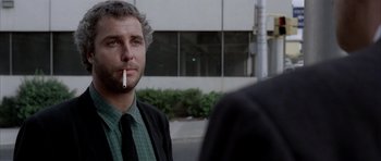 Movie still from “Manhunter” (1986), directed by Michael Mann – A man smoking a cigarette while standing next to another man; Close Up shot, Over the shoulder angle