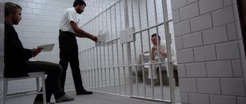 Movie still from “Manhunter” (1986), directed by Michael Mann – A man in a jail cell with another man in a jail cell behind bars; Wide shot, High angle