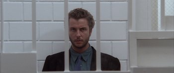 Movie still from “Manhunter” (1986), directed by Michael Mann – A man in a suit and tie behind bars; Close Up shot, Low angle