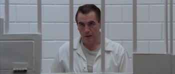 Movie still from “Manhunter” (1986), directed by Michael Mann – A man sitting in front of a white wall behind bars; Close Up shot, Low angle