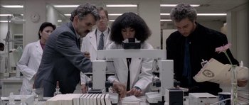 Movie still from “Manhunter” (1986), directed by Michael Mann – A woman in a white lab coat is looking at a book; Medium shot, Low angle