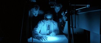 Movie still from “Manhunter” (1986), directed by Michael Mann – A man in a white lab coat looking at a light; Medium shot, Low angle