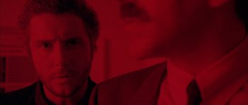 Movie still from “Manhunter” (1986), directed by Michael Mann – A man in a suit and tie in front of a red wall; Extreme Close Up shot, Over the shoulder angle