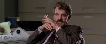 Movie still from “Manhunter” (1986), directed by Michael Mann – A person wearing a suit smoking a cigarette; Close Up shot, Low angle