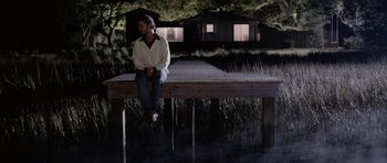 Movie still from “Manhunter” (1986), directed by Michael Mann – A man sitting on a dock at night; Wide shot, Over the shoulder angle