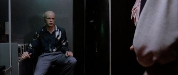 Movie still from “Manhunter” (1986), directed by Michael Mann – A man sitting on a chair in front of a door; Medium shot, Low angle