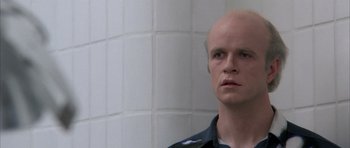 Movie still from “Manhunter” (1986), directed by Michael Mann – A man with a bald head standing next to a white wall; Close Up shot, Low angle