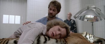 Movie still from “Manhunter” (1986), directed by Michael Mann – A woman laying on the ground in a room with two men; Medium shot, Low angle