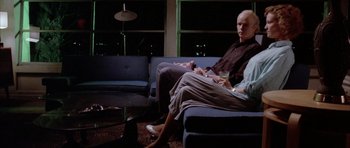 Movie still from “Manhunter” (1986), directed by Michael Mann – A man and woman sitting on a blue couch in a living room; Wide shot, High angle