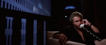 Movie still from “Manhunter” (1986), directed by Michael Mann – A man sitting on top of a couch in front of a tv; Medium shot, Low angle