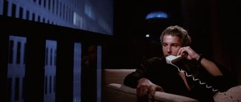 Movie still from “Manhunter” (1986), directed by Michael Mann – A man sitting on top of a couch drinking a cup of coffee; Medium shot, Low angle